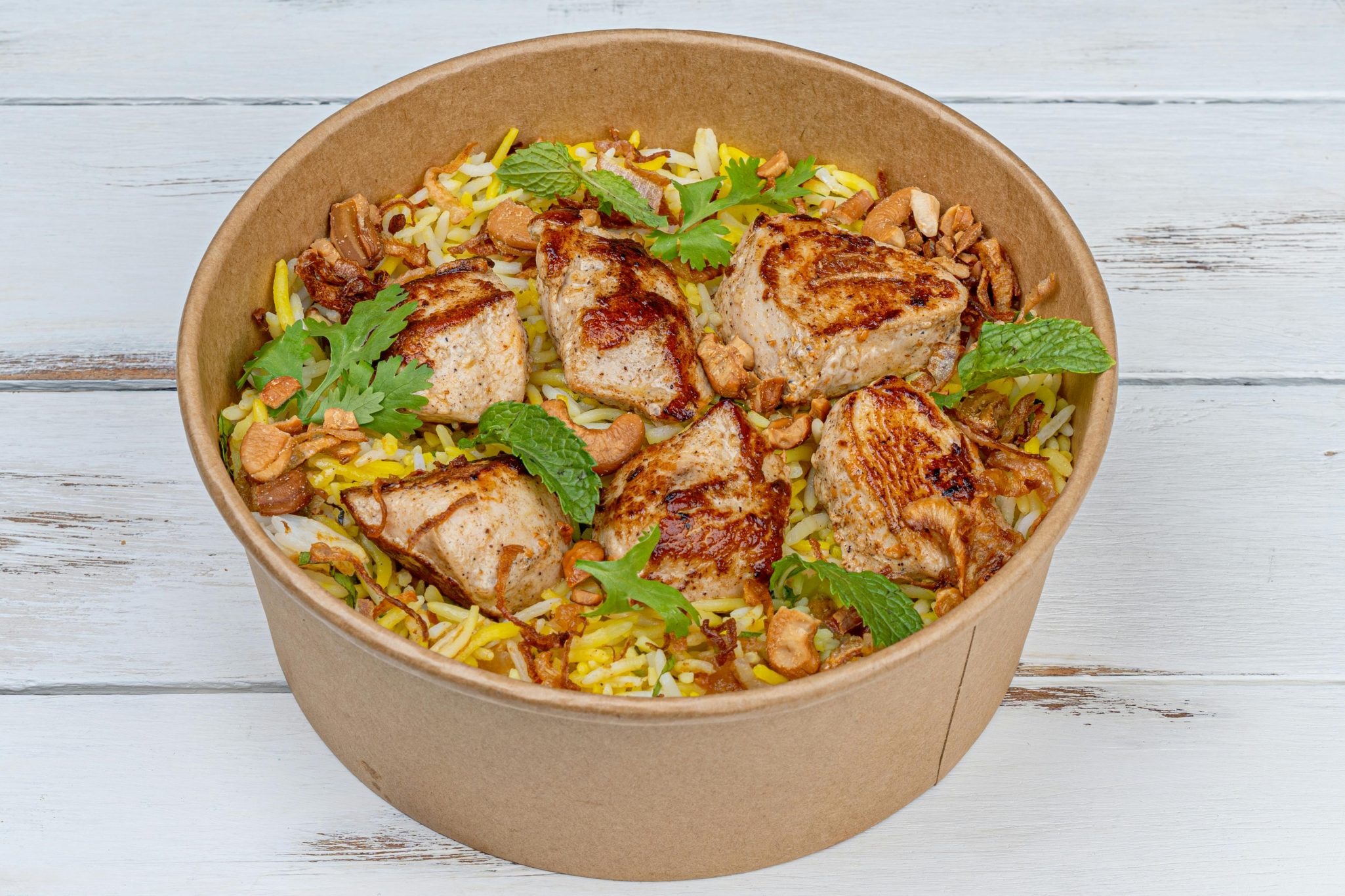 A delicious serving of grilled chicken biryani topped with herbs and nuts in an eco-friendly bowl.