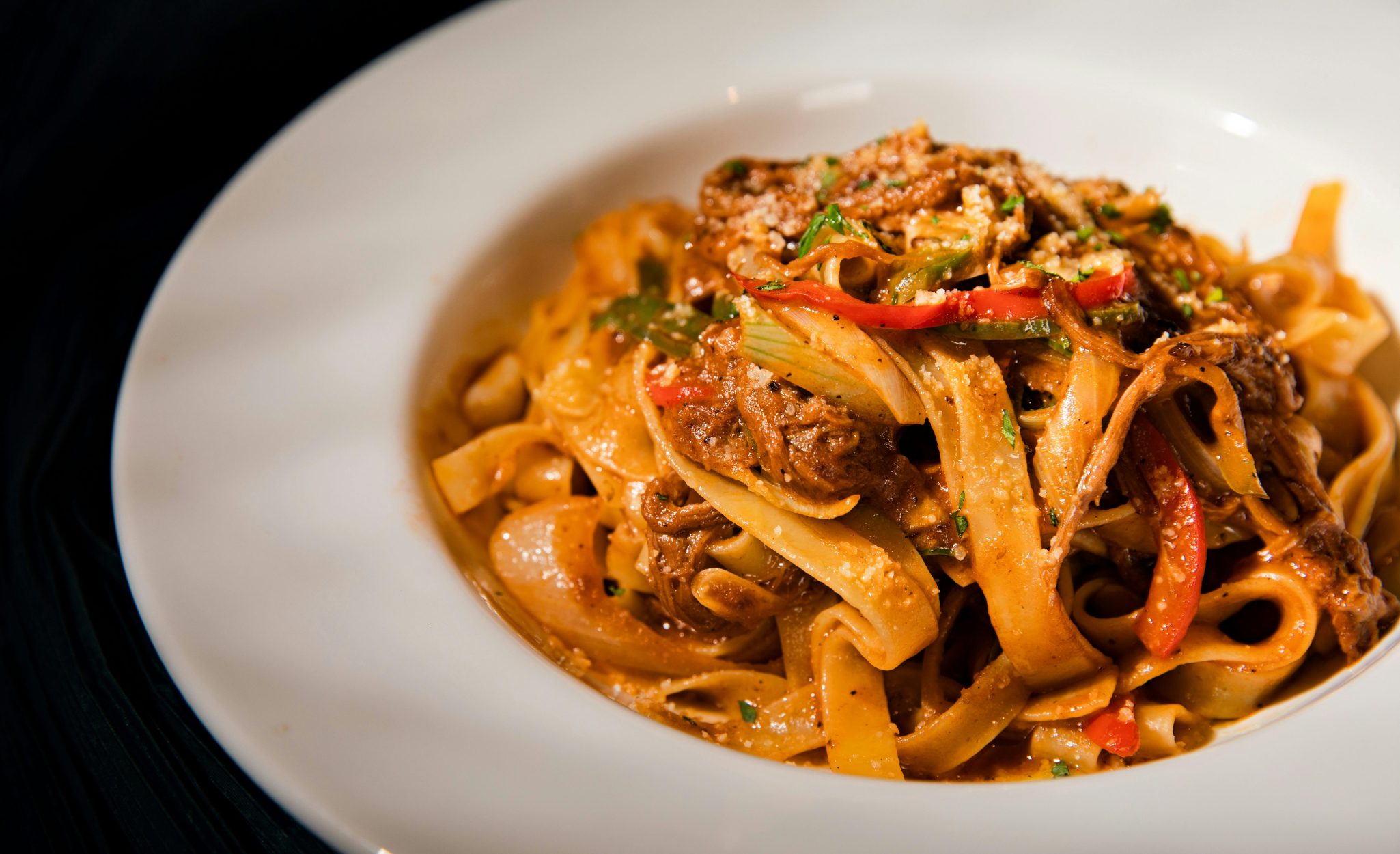 Savory beef tagliatelle pasta with peppers and herbs in a white plate, perfect for a gourmet meal.