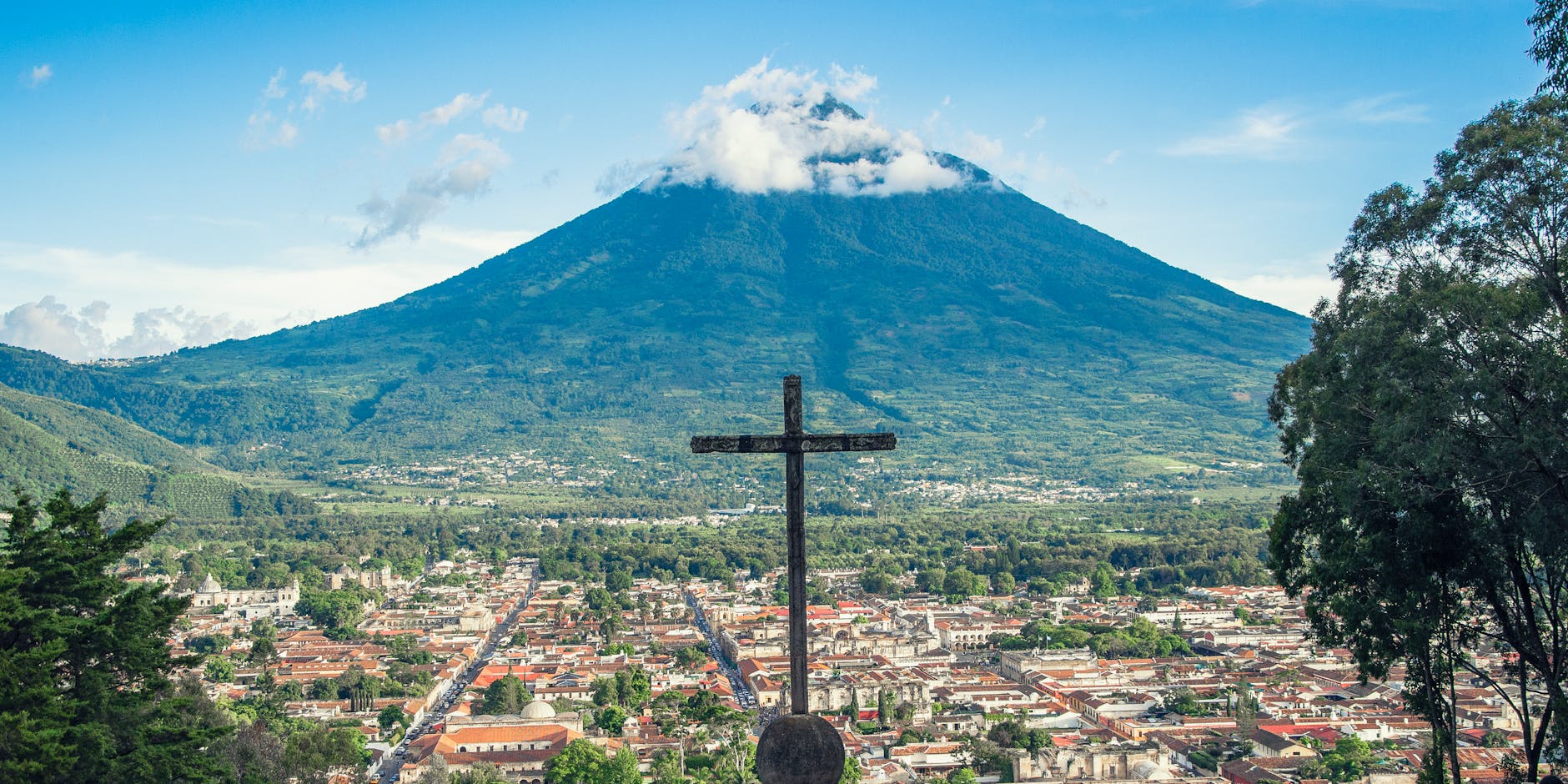 Scenic view of Antigua Guatemala with Volcán de Agua, featuring a prominent cross in the foreground.