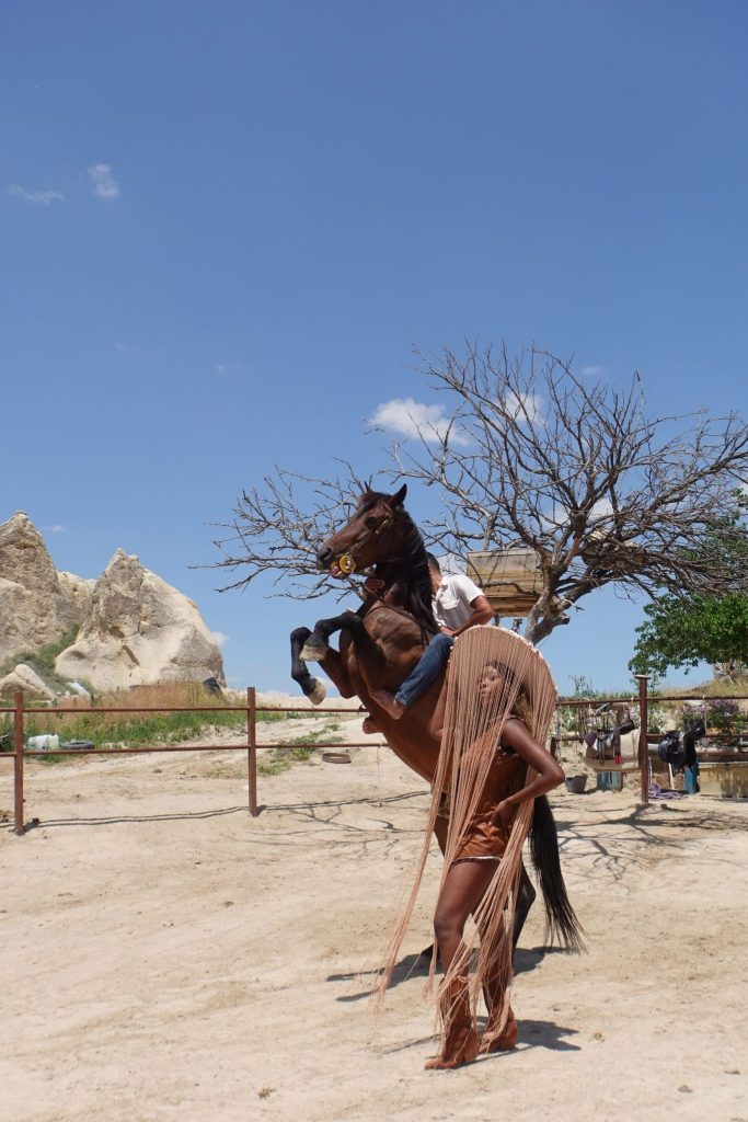 Girl wearing a hat with fringes pose next to a horse kicking it's two front feet up