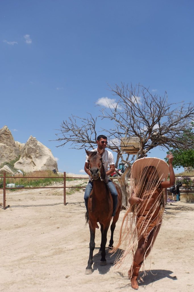 Girl wearing a hat with fringes pose next to a horse kicking it's two front feet up
