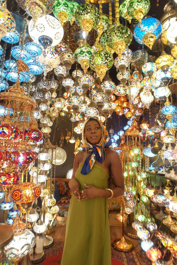 Black girl wearing a scarf, staring up into a room filled with Turkish lamps