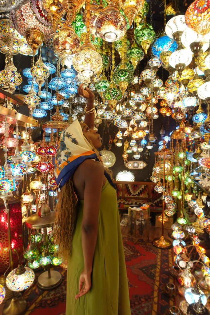 Black girl wearing a scarf, staring up into a room filled with Turkish lamps
