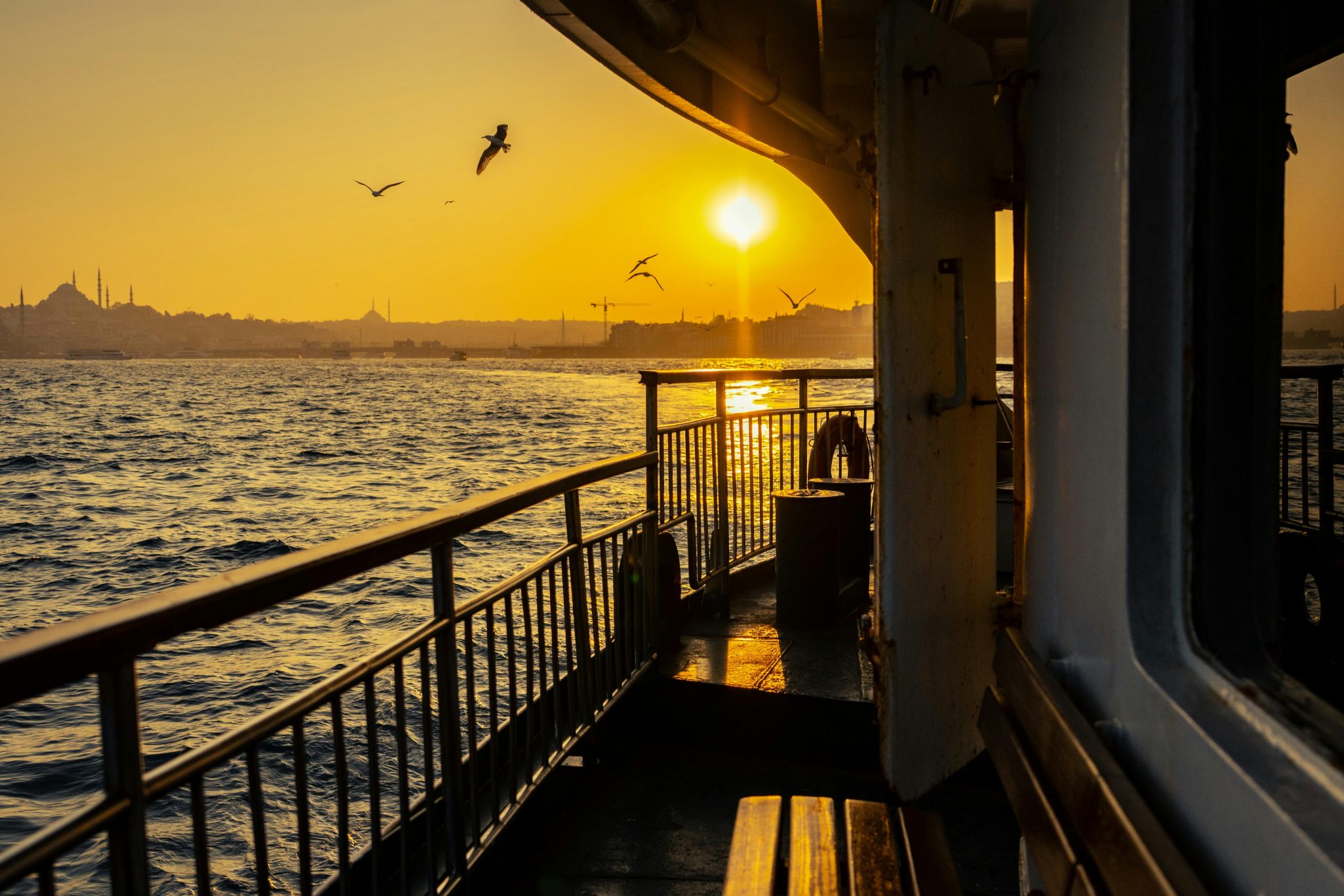 Golden sunset over the Bosphorus with seagulls and iconic Istanbul skyline viewed from a boat.