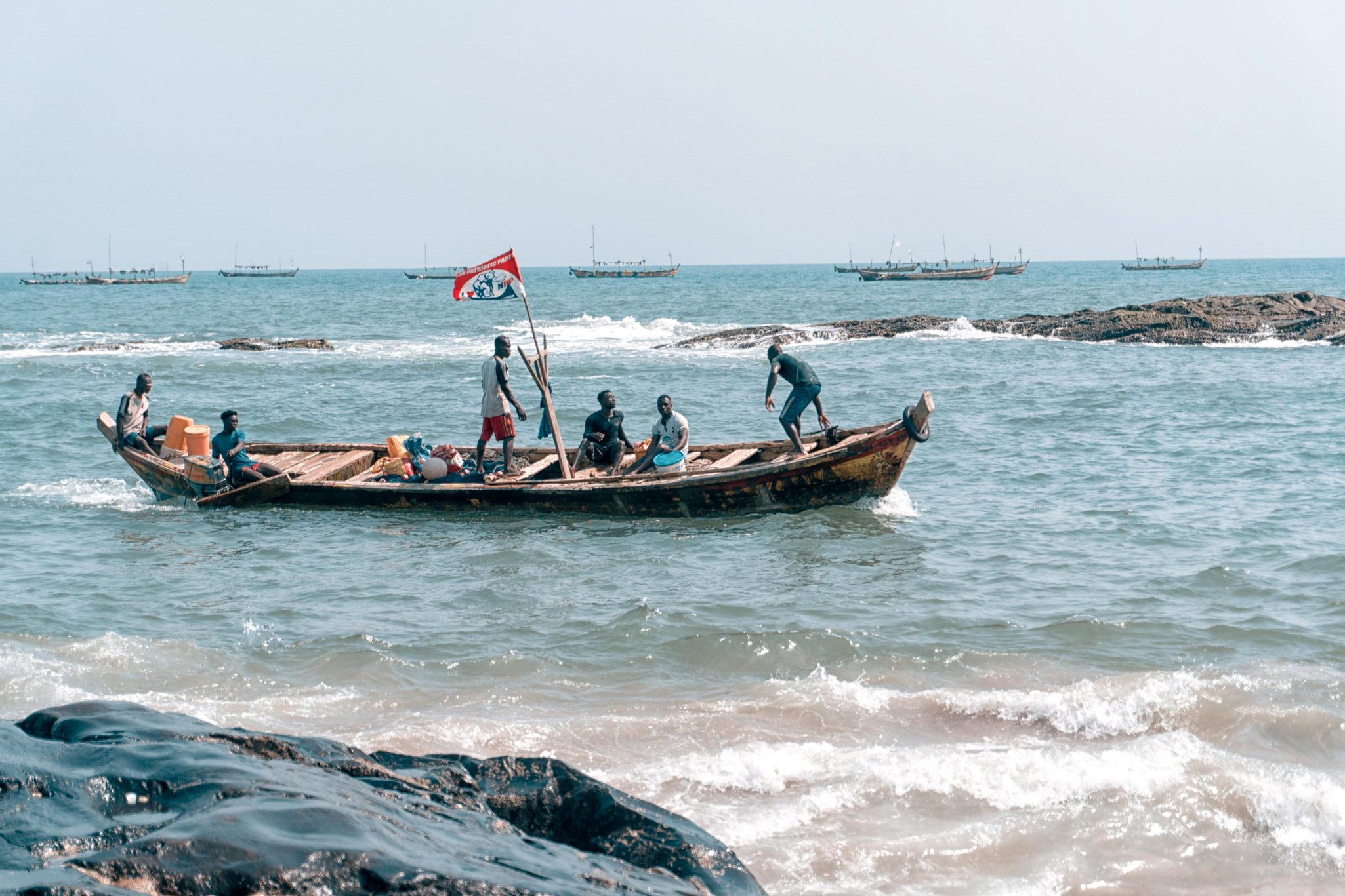 Fishermen navigating a wooden boat on the vibrant Elmina coast, showcasing traditional fishing culture in Ghana.