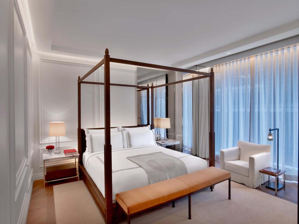 A luxurious hotel room featuring a four-poster bed, stylish seating, and modern decor with large windows allowing natural light.
