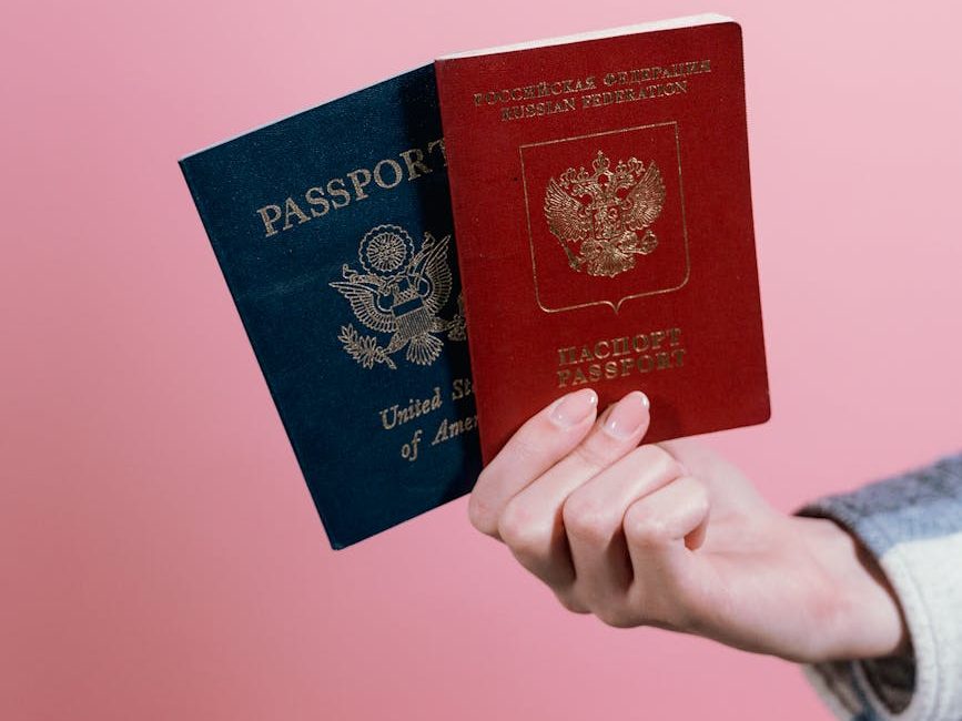 Close-up of two passports held by a hand against a pink background.