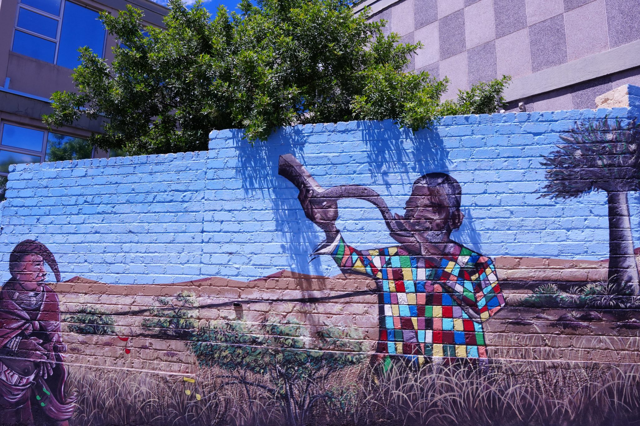 A colorful mural depicting a man playing a horn, wearing a checkered shirt, with a background of grass and hills.