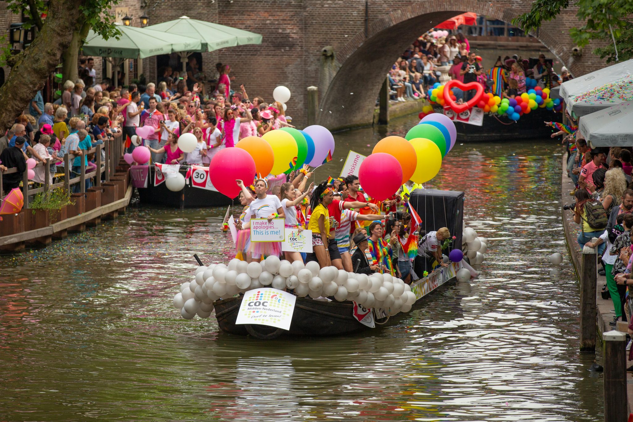 Vibrant pride parade on Utrecht's canal with crowds celebrating diversity in a festive atmosphere.